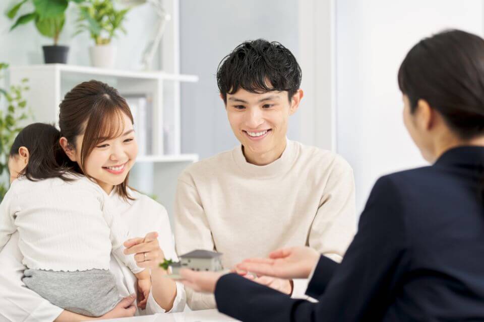 小さなお子様を抱えたご夫婦が、担当者と家の模型を見ながら笑顔で相談している様子